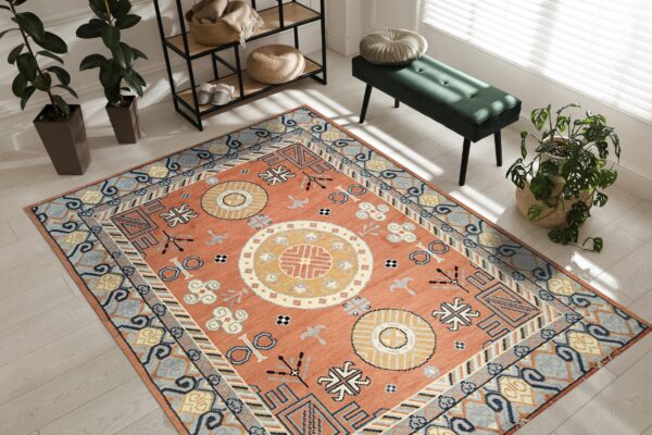 Burnt orange rug with blue and yellow geometric patterns on light wood flooring next to a dark green bench.