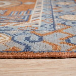 Geometric patterned rug in shades of blue and rust with low pile resting on light wood floor.