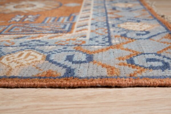 Geometric patterned rug in shades of blue and rust with low pile resting on light wood floor.