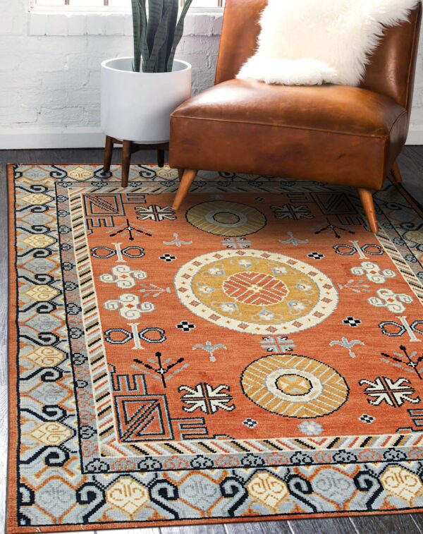 Burnt orange rug with geometric medallions and tribal designs sits on dark wood floor.