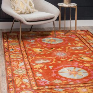 Ornate orange and multi-colored floral rug displayed under a modern gray chair and brass side table.