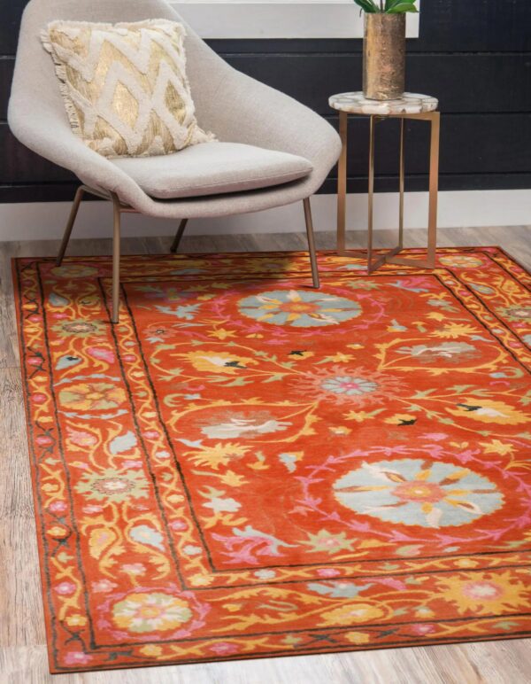 Ornate orange and multi-colored floral rug displayed under a modern gray chair and brass side table.