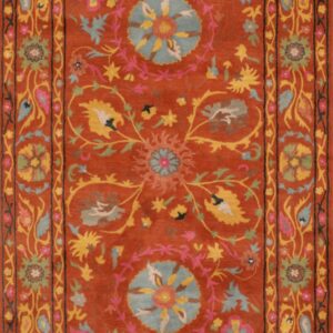 Rust-colored rug featuring a dense floral medallion and vine pattern in teal, yellow, pink, and green accents.