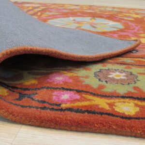 Rolled back rug corner reveals the gray backing and thick pile with orange, pink, and green floral patterns.