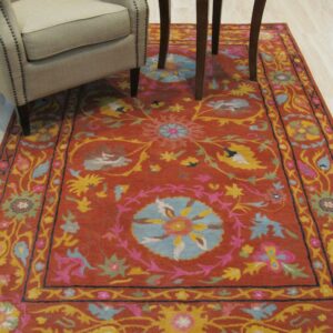Textured rust rug with a bright multicolored floral medallion pattern next to a beige upholstered armchair.