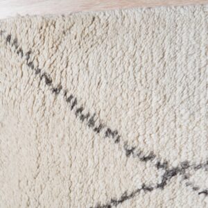 High-pile cream rug with irregular gray lines and fringe rests on light wood flooring.