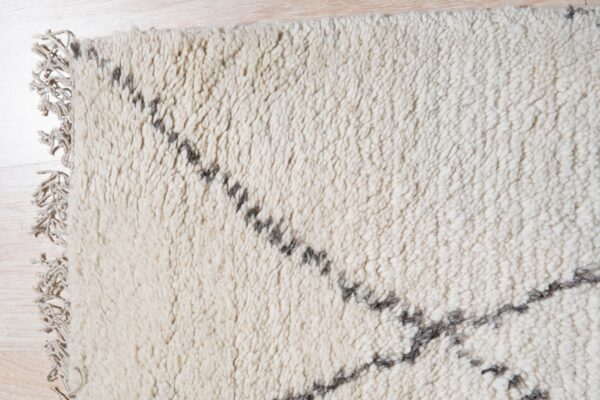 High-pile cream rug with irregular gray lines and fringe rests on light wood flooring.