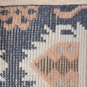 Highly textured blue, cream, and peach geometric rug lying on light wood flooring.