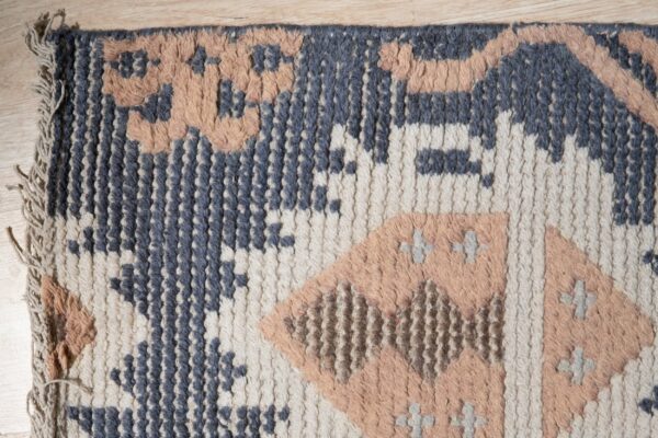 Highly textured blue, cream, and peach geometric rug lying on light wood flooring.