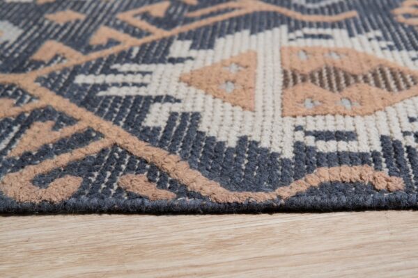 A close-up of a multi-textured geometric rug in dark gray, cream, and raised beige resting on wood flooring.