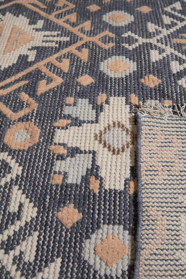 Geometric rug texture in slate, cream, and salmon with raised motifs, folded to show the backing.