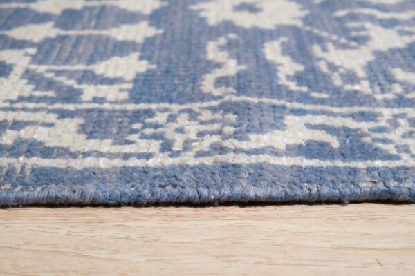 Thick-piled blue and off-white rug edge with abstract pattern rests on light wood grain.