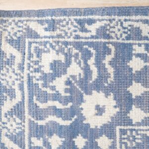 Textured blue and white rug corner with geometric patterns and fringe visible on light wood floor.