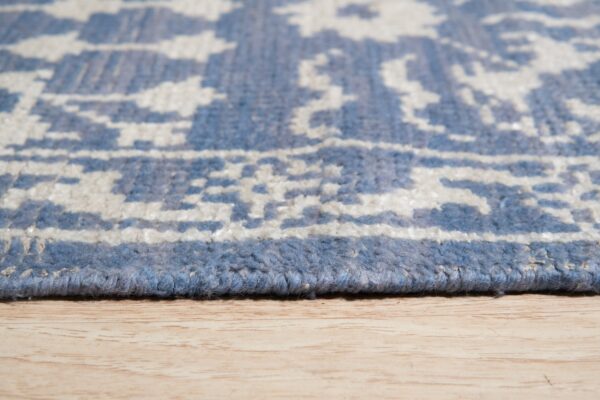 Close-up of a blue and off-white patterned rug edge and chunky pile resting on light wood flooring.