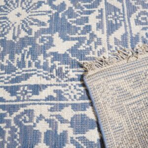 Textured blue and cream geometric patterned rug with a fringed edge folded back showing the woven reverse.