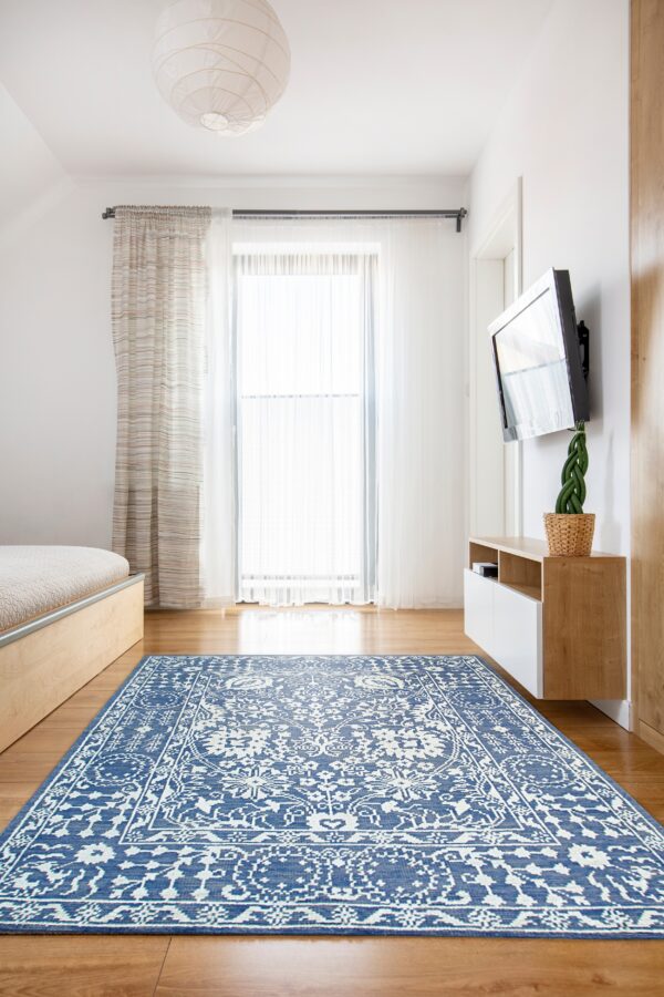 Blue and white ornate rug lies on a hardwood floor in a brightly lit room with white walls.