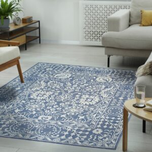 Low-pile blue and white traditional pattern rug on light wood floors beside a neutral sectional sofa.