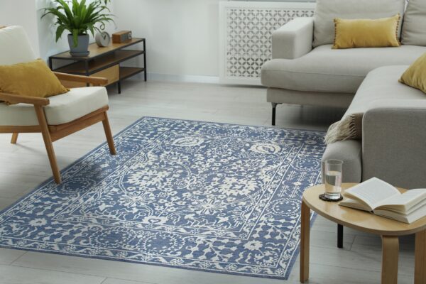 Low-pile blue and white traditional pattern rug on light wood floors beside a neutral sectional sofa.