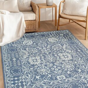 A blue and white traditional patterned rug on hardwood floors, framed by wicker furniture and a small wooden side table.