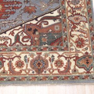 Ornate patterned rug in slate blue, terracotta, and cream sits on pale blonde wood plank flooring.