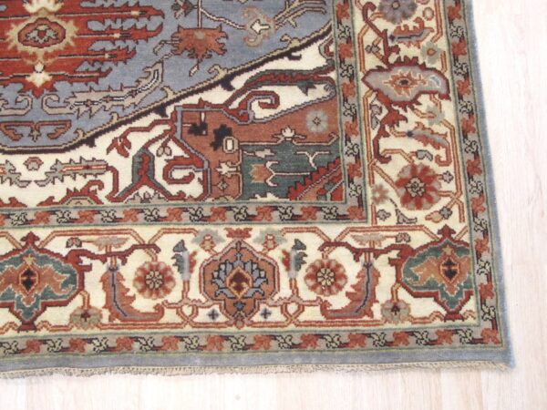 Ornate patterned rug in slate blue, terracotta, and cream sits on pale blonde wood plank flooring.