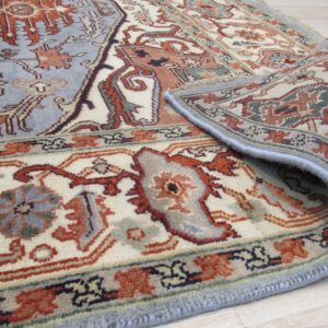 A blue and rust patterned rug with cream details is partially rolled back on a light wood floor.