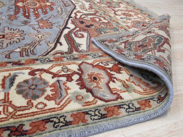 A blue and rust patterned rug with cream details is partially rolled back on a light wood floor.