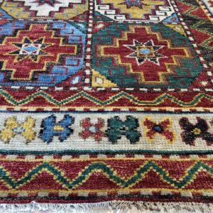 Textured rug in red, gold, and teal with detailed geometric tribal motifs on light wood.