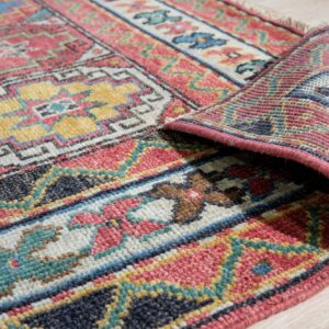 Multicolor geometric patterned rug corner is rolled back, displaying the woven texture on pale wood flooring.