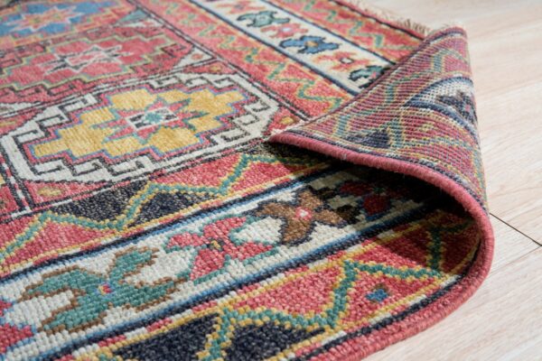 Multicolor geometric patterned rug corner is rolled back, displaying the woven texture on pale wood flooring.