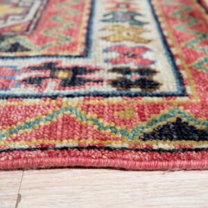 Angled view of a textured rug featuring red, blue, cream, and teal geometric borders on blonde flooring.