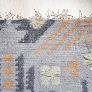 Textured gray rug with thick pile, abstract dark gray, peach, and off-white shapes on light wood.