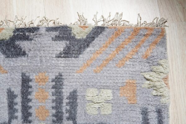 Textured gray rug with thick pile, abstract dark gray, peach, and off-white shapes on light wood.