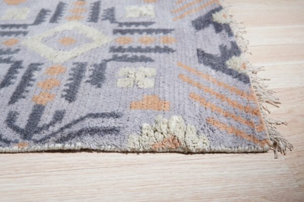 High-pile lavender and neutral geometric rug with fringe rests on light wood plank flooring.