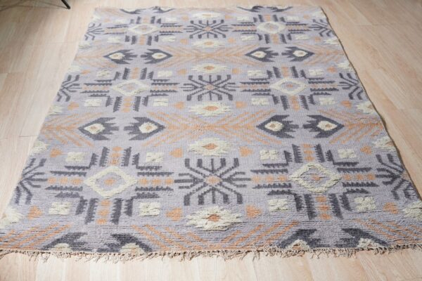 High-pile lavender rug with charcoal, cream, and apricot geometric motifs on light wood floor.