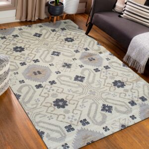 Beige rug featuring gray, taupe, and dark blue abstract medallions placed on hardwood floors near a dark sofa.