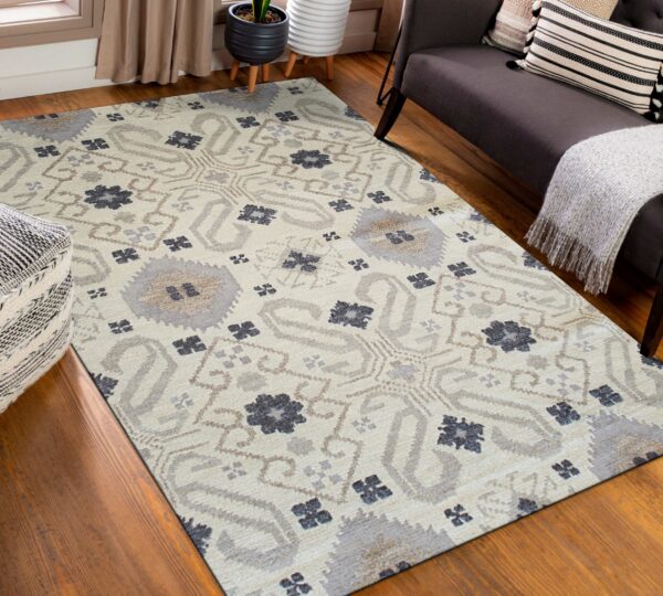Beige rug featuring gray, taupe, and dark blue abstract medallions placed on hardwood floors near a dark sofa.