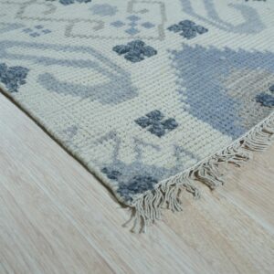 Geometric cream rug featuring light blue and slate gray motifs with visible fringe on light wood floor.