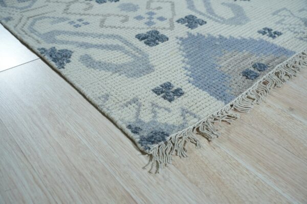 Geometric cream rug featuring light blue and slate gray motifs with visible fringe on light wood floor.