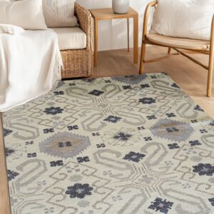 Beige patterned rug featuring gray and dark blue motifs placed between wicker sofa and wood armchair.