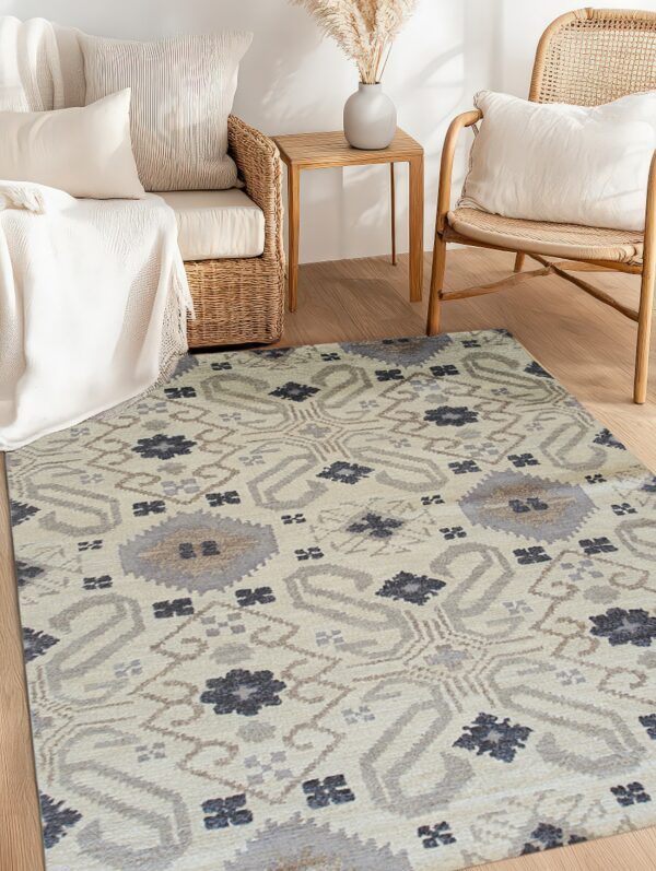 Beige patterned rug featuring gray and dark blue motifs placed between wicker sofa and wood armchair.