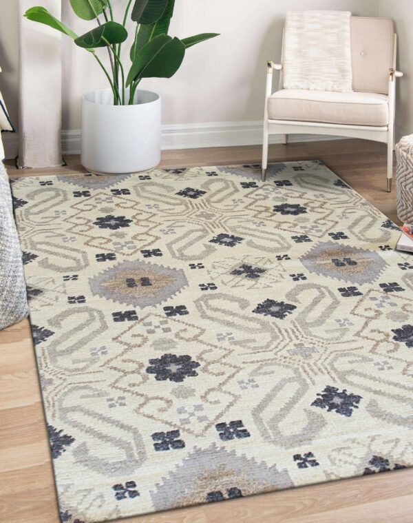Neutral rug with gray, cream, and dark blue geometric patterns on wood floors beside a white chair and plant.