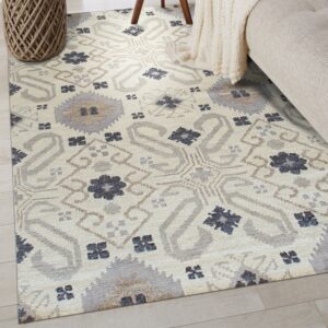 Light beige geometric rug featuring grey, taupe, and dark blue patterns on pale plank flooring.