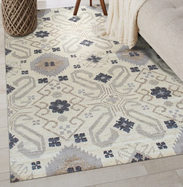 Light beige geometric rug featuring grey, taupe, and dark blue patterns on pale plank flooring.