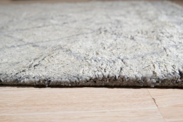 Light beige high-pile rug with faint gray abstract lines sits on blonde wood planks.