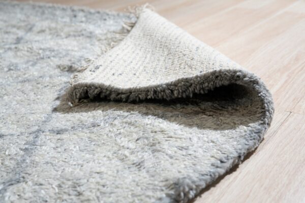 Shaggy white and gray rug rolled back to reveal its backing on light wood flooring.