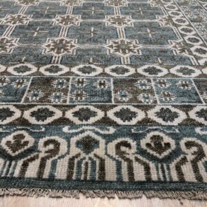 Low-angle view of a textured rug in teal, brown, and cream geometric patterns on wood plank flooring.
