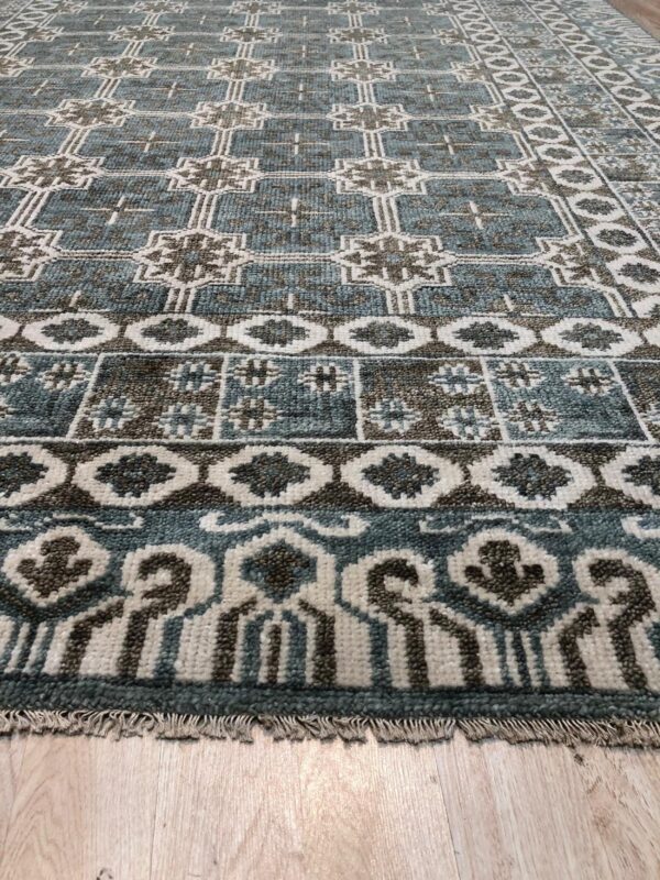 Low-angle view of a textured rug in teal, brown, and cream geometric patterns on wood plank flooring.