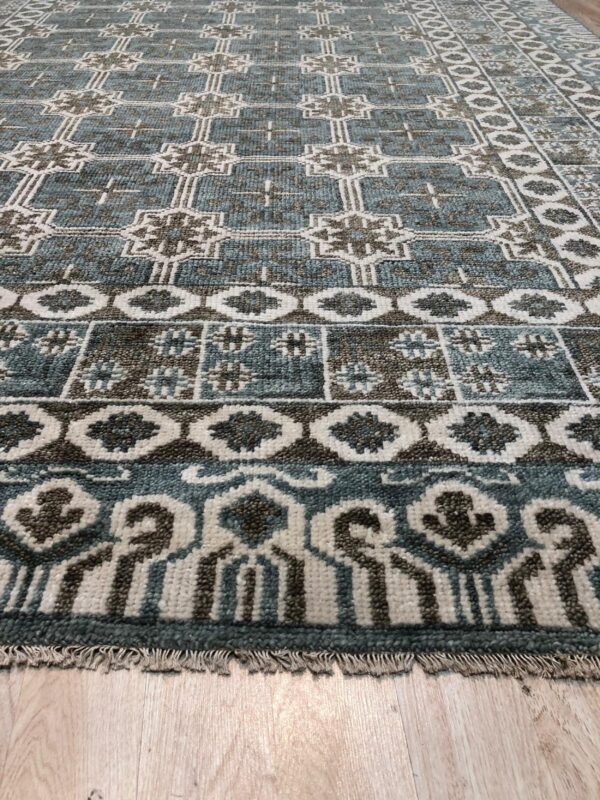 Blue and brown rug with dense geometric patterns and fringes resting on light wood floors.