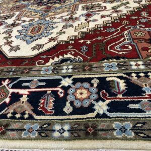 Cream rug featuring traditional geometric and floral designs in red, navy, blue, and tan on wood floors.